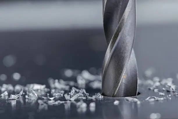 metal drill bit make holes in steel billet on industrial drilling machine with shavings. Metal work industry. multi cutting tool and end mill.