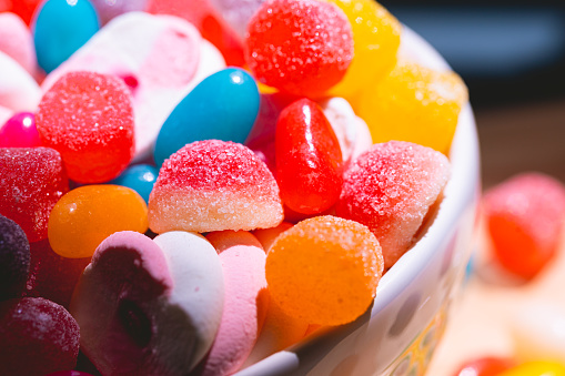 Candy. Assorted sweets in a bowl and on a wooden board. Among them: marshmallow drops and gum.