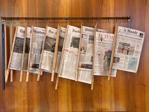 Sils Maria, Swizerland - August, 24 - 2022: International newspapers hanging at a wooden wall in a public library.