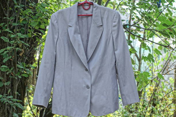 one gray old jacket made of fabric hangs on a red hanger and a wire in the street among green vegetation