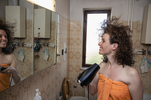 Curly Hair Mid Adult Serene Woman Dries her Hair in front of the Mirror in her Home Domestic Bathroom