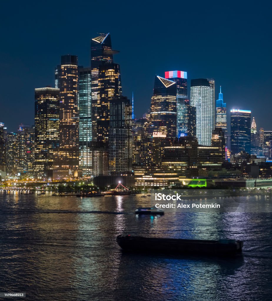 Hudson Yards with modern condos, seen from the Hudson River, illuminated at night. Hudson Yards, illuminated at night. Yacht going along the Hudson River. New York City Stock Photo