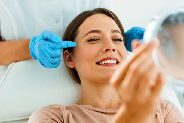 hermosa mujer en tratamiento facial mirando al espejo - attractive female human collagen syringe injecting fotografías e imágenes de stock