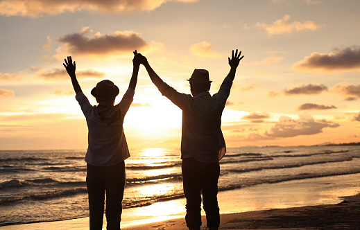 Silhouette couple enjoy elderly relaxation on the beach against sunset or sunrise sky