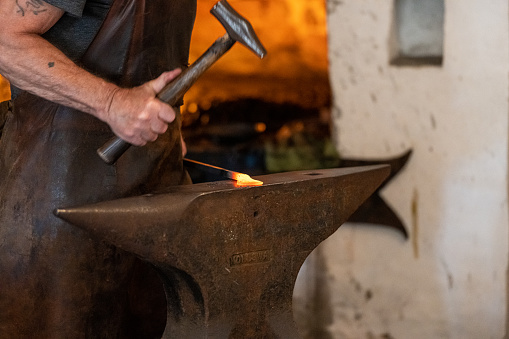 Varberg, Sweden - July 04 2022: Blacksmith hammering on red hot iron on a large anvil.
