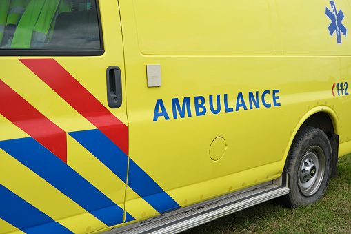 Dutch Ambulance logo on the side of a parked medical van. Ambulance sign on yellow vehicle with red and blue stripes.