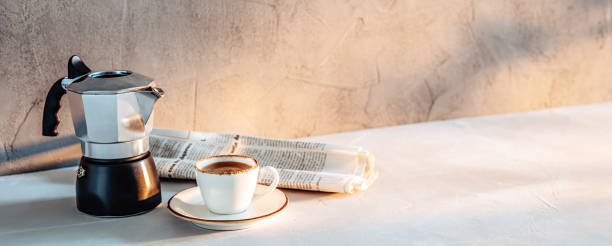 A cup of espresso, a coffee maker and a newspaper in the morning sunlight stock photo