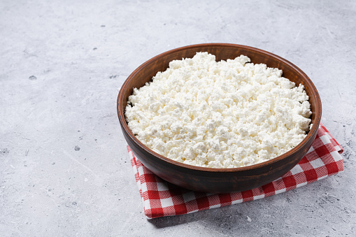 Cottage curd cheese in a wooden bowl grey table background. Homemade milk food. Top view