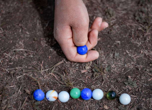istock Child playing with marbles on yhe sidewalk. Old-fashioned toys still in use today. 1419700954
