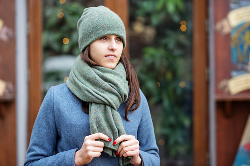 Portrait of a girl in a green hat and scarf, a walk through the Christmas city, a smile on her face, cool weather, a fascinating looking off to the side.