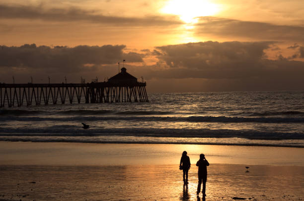 Sunset at Huntington Beach pier in California with a silhouette of a surfer.