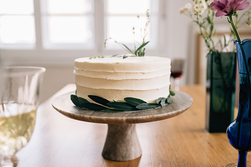 A white homemade cake decorated by leaves prepared for some celebration.