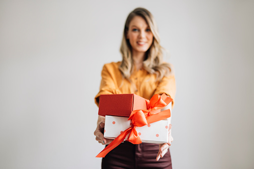 A portrait of a smiling Caucasian female giving beautifully wrapped gifts tied with ribbons.