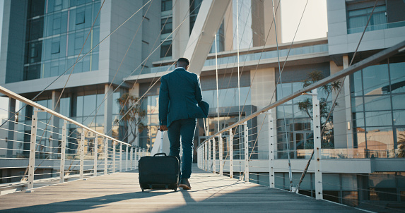 Travel, hotel and businessman walking with his luggage towards airport or office building in the city. Male entrepreneur going on business trip and arriving at destination for new career opportunity