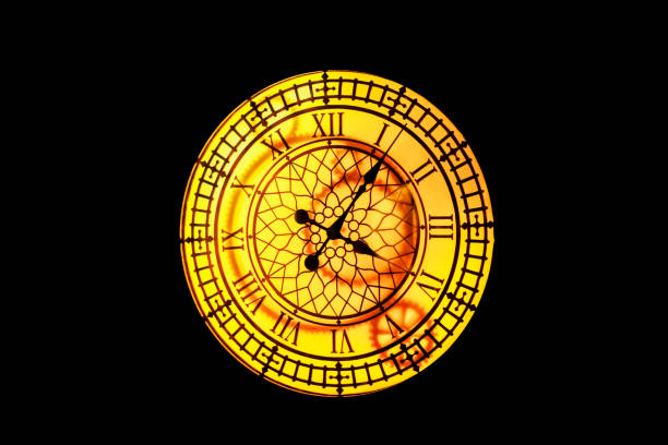 Glowing vintage yellow clock with roman dial on dark wall. Blurred image.