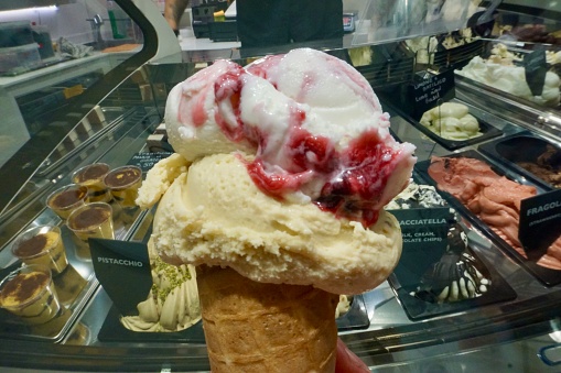 Pistachio -cherry Italian ice cream in a waffle cone in Venice. Ice cream on the background of other types of ice cream in Italy.
