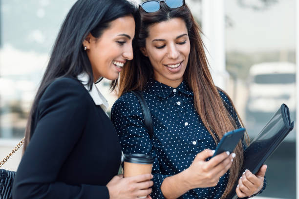 istock Two beautiful businesswomen using smart phone while drinking coffee walking around the city. 1419724035