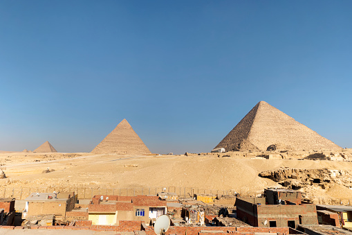 The great pyramid of Cheops in Cairo, Egypt. Pyramids of Khafra against the blue sky. Old residential buildings of the poor quarter of Giza, Egypt.