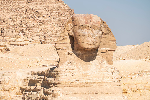 closeup of the face of the Great Sphinx with pyramid in the background on a beautiful blue sky day in Giza, Cairo, Egypt.