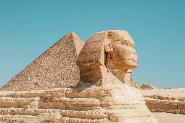 great sphinx including head, feet with pyramid of menkaure in background on clear, blue sky day in giza, egypt empty with no people. - giza pyramids sphinx pyramid shape pyramid imagens e fotografias de stock