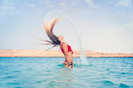 A girl is having fun. A blonde girl in a red swimsuit splashes in turquoise water at the resort against a blue cloudy sky.