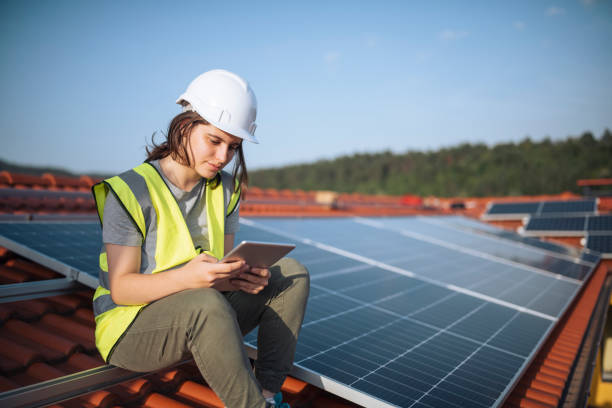 Female engineer sitting on a rooftop with solar panels using technology. stock photo