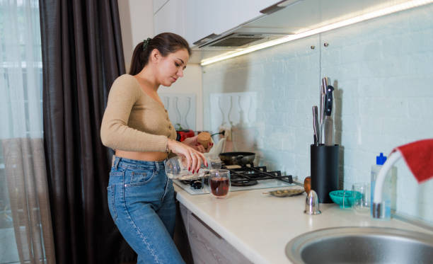 istock Young woman is preparing tea in the modern kitchen. She uses a tea bag and makes it directly in a cup. 1419735564