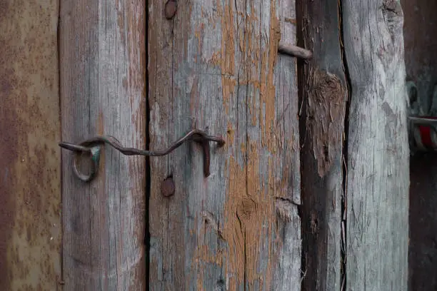 Photo of An old brass hook closes a dilapidated door on an old dilapidated wooden shed.