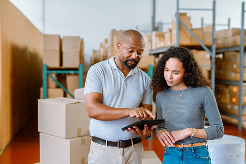 Logistics courier worker and employee with a tablet for online delivery in warehouse. Service man with box, package and business woman working on a digital management app or notification information