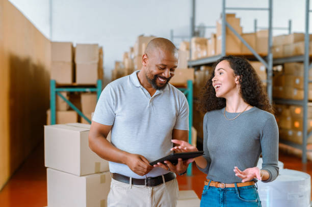 istock Manager checking stock on a digital tablet while talking to a coworker at a logistics warehouse. Man and woman discussing package shipping delivery. Team speaking and working on technology at factory 1419741128