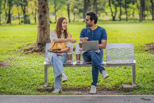 business people or university students sitting on bench working together outdoor in park. Concept of workation and digital nomads lifestyle