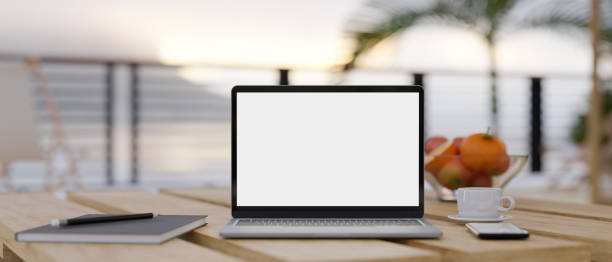 istock Notebook laptop mockup and stuff on wooden table over blurred sea view in the background. 1419765719