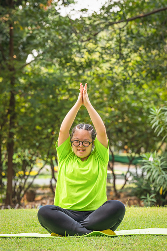 happy asian young woman with down syndrome or autism exercising and doing yoga outdoors in park