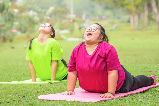 asian young woman with down syndrome or autism with friend exercising and doing yoga outdoors in park together