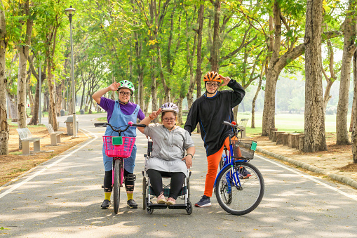 group of Asian friends with down syndrome riding bicycle and wheelchair for exercise together outdoors in park