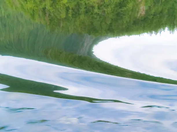Abstract patterns of forest and curves and swirls on calm water surface in Alaska.