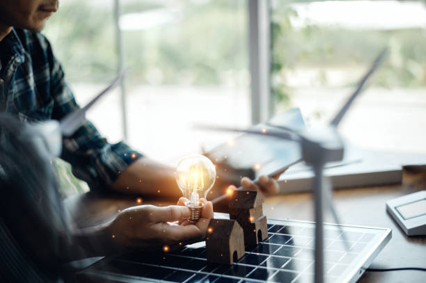 istock An engineer sits holding a light bulb and a tablet looking at a model of a house. with solar panels and a model house on the table. To design use of renewable energy with wind and solar energy. 1419789900