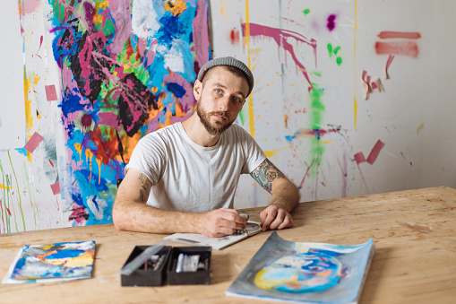 A bearded artist works in his sketchbook in his abstract painting art studio