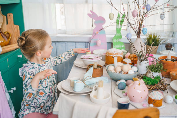 istock Girl at table with Easter decoration. Celebration in kitchen.Tablescape for home Easter holiday.Family religious traditional festive christianity,catholic food.Colored eggs,cake,fun bunny,candy sweet 1419792663