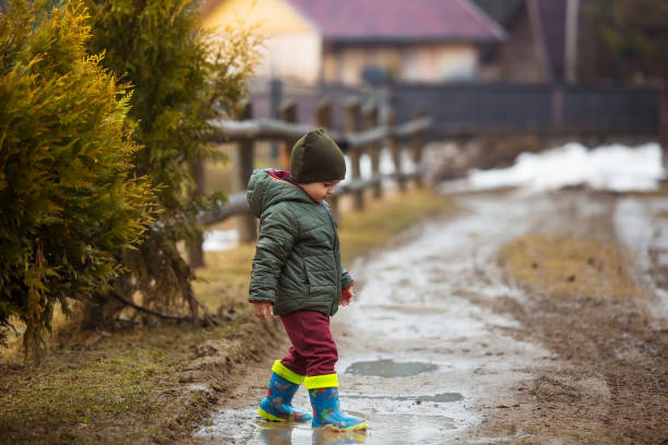 istock Little boy in protective rubber boots and rain clothes jumping in mud puddle. Happy child having fun while playing in puddle after rain. 1419797635