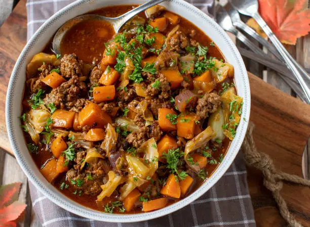 Delicious stew with autumn and winter season cooked with ground beef, cabbage, carrots, onions and herbs. Served in a rustic bowl on wooden background