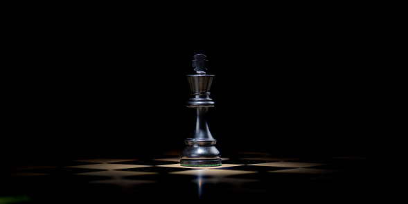 Close-up of black king chess piece on chessboard against black background.