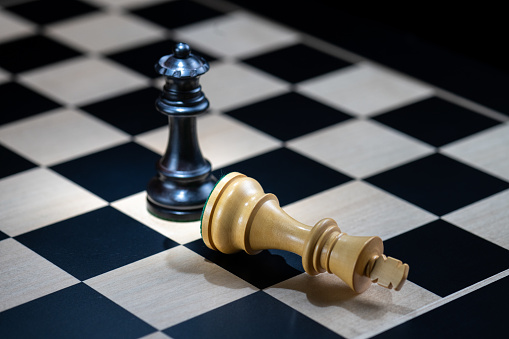 Close-up of king and queen chess pieces on chessboard against black background.