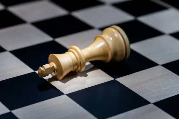 Close-up of cream coloured king chess piece checkmate.