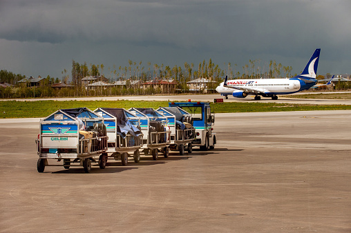 Ankara, Turkey - May 1, 2014 : Cargo transport trolley belonging to Çelebi Aviation Holding is moving along the apron with the cargoes. AnadoluJet plane is about to take off.
