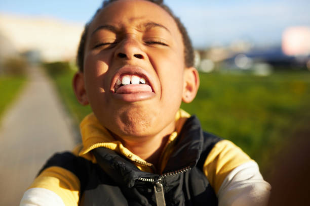 lustiges selbstporträt von afroamerikanischen jungen kind grimassen, mainbg gesichter spielen woith smartphone kamera machen selfie im freien wjile im park gehen. kinder und technologie, gadgets und kindheit - making a face child humor human face stock-fotos und bilder
