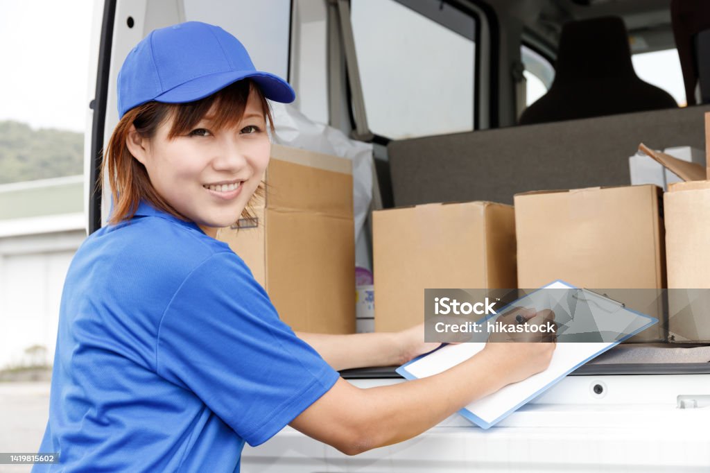 A female driver of light cargo is filling out paperwork. She is wearing a blue polo shirt and cap. Home Delivery Stock Photo