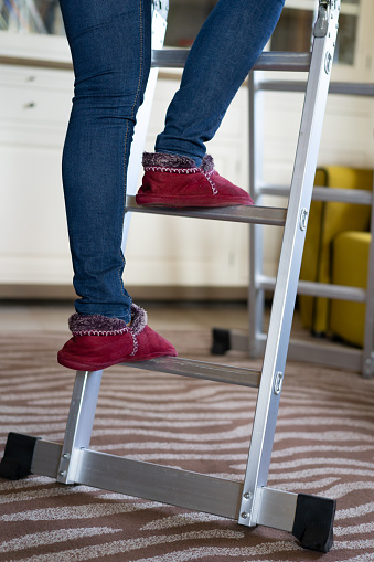 Woman with  slippers climbing on a ladder at home