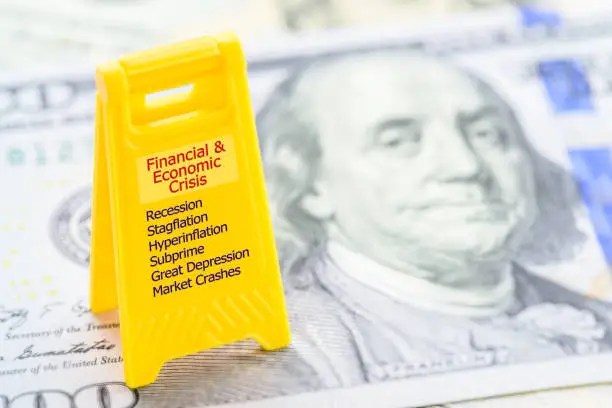 Financial and economic crisis concept : Small yellow sign board on a US dollar banknote, an economic or a financial crisis occurs when financial assets lose a large portion of their nominal value.