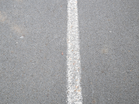 Parallel lines of road marking, asphalt and grassy verge.
